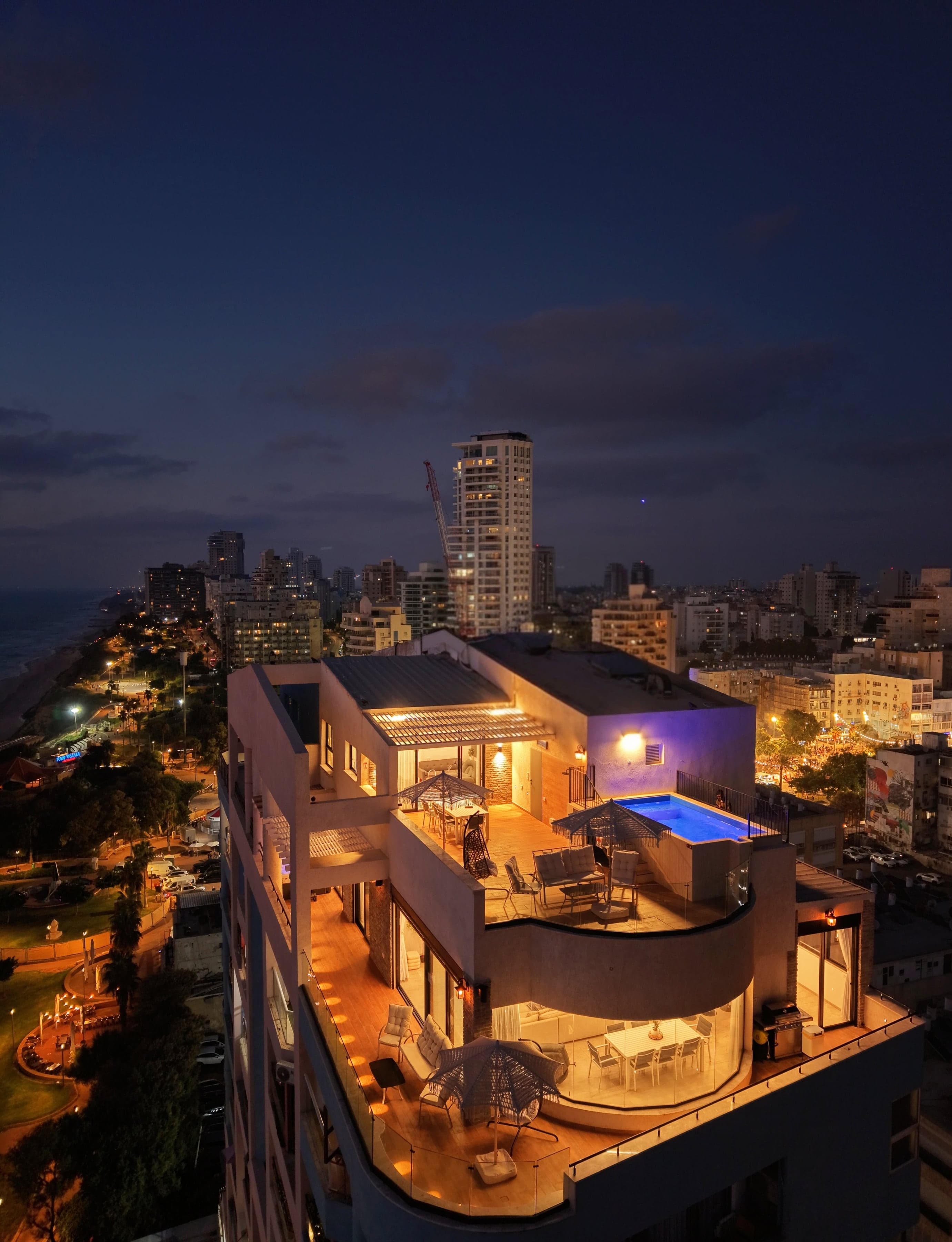SEA VIEW בדמדומים מעל הטיילת וחוף הים של נתניה, עם הבריכה המוארת על הגג