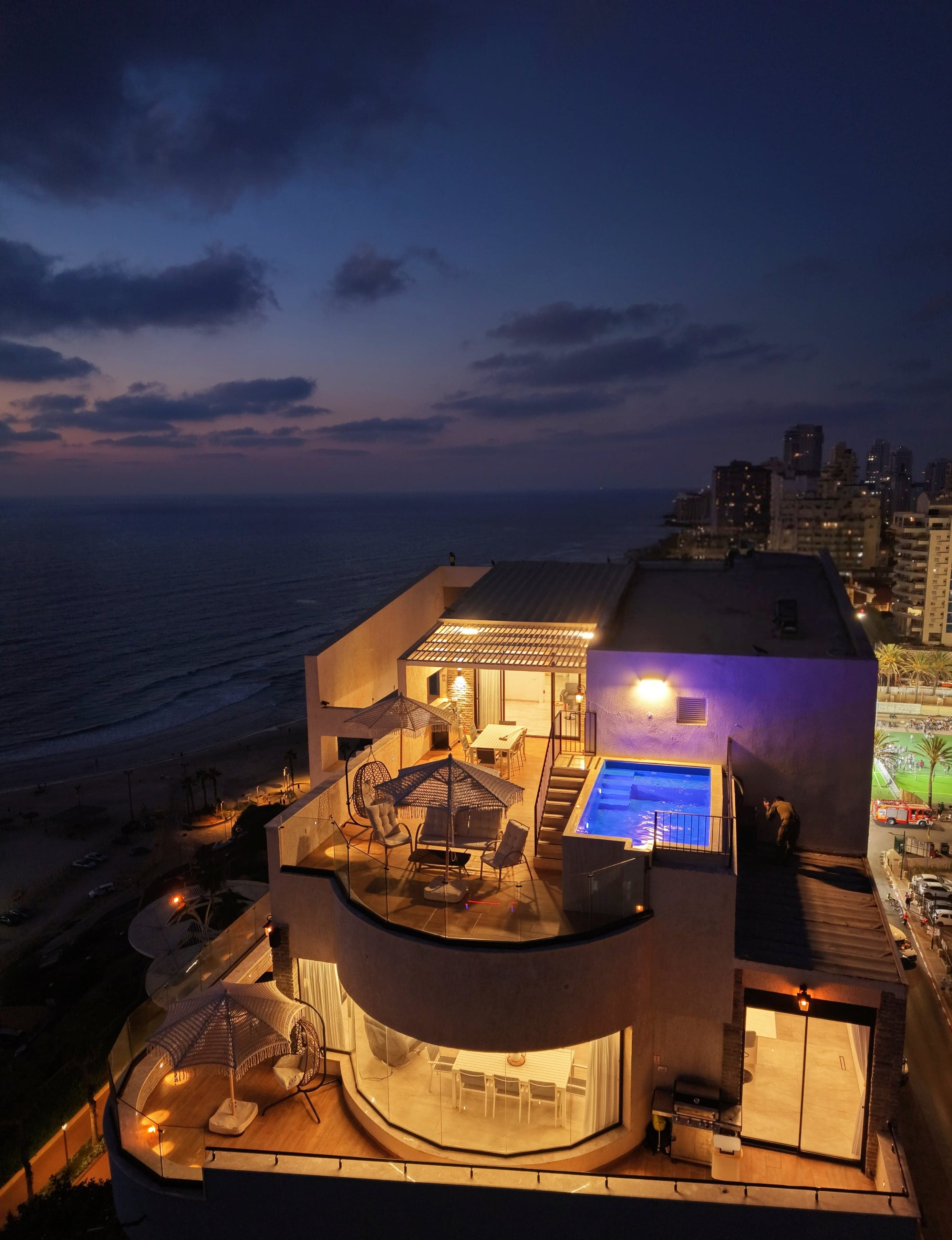 מתחם SEA VIEW עם הבריכה המחוממת המוארת על הגג, מול הים התיכון בשעת שקיעה